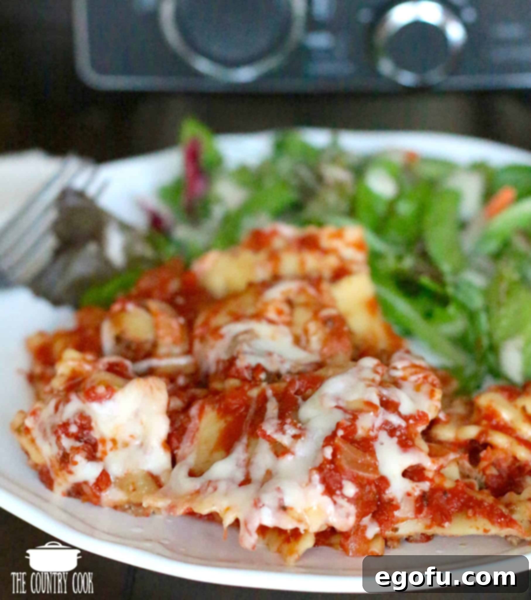 Cooked ravioli, homemade marinara sauce, melted mozzarella cheese, on a white plate with a green salad and a Ninja slow cooker in the background, showcasing a complete meal.