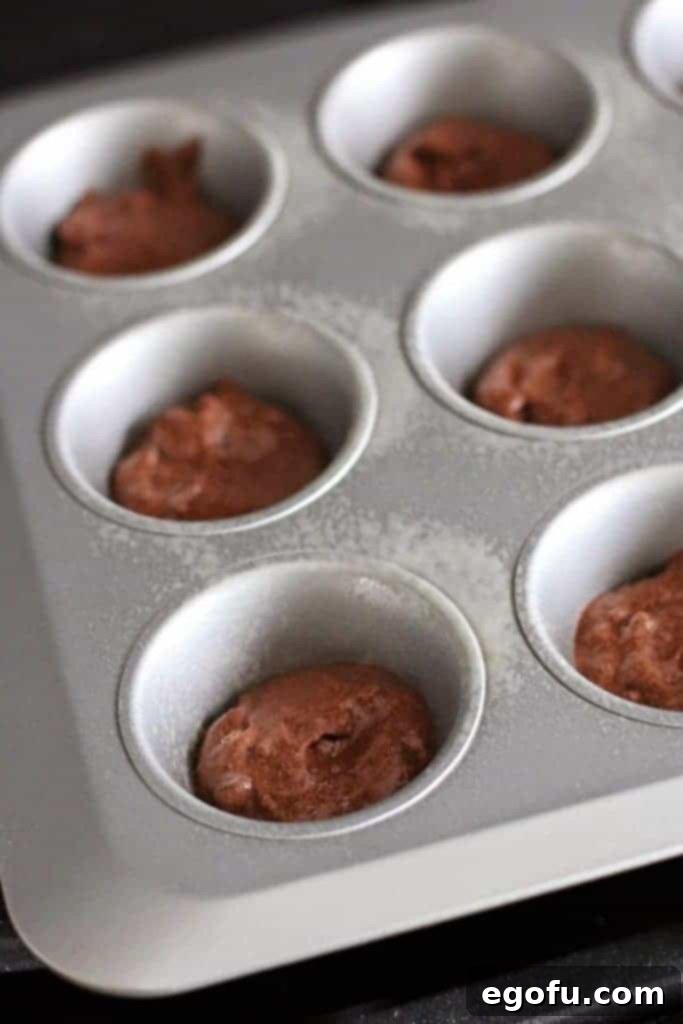 Chocolate muffin batter carefully poured into the bottom of each cup in a muffin tin.