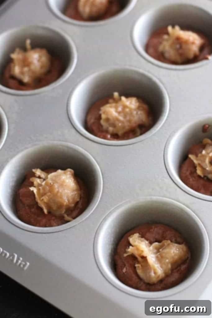 Coconut pecan frosting dolloped on top of the chocolate muffin batter, ready for the next layer.