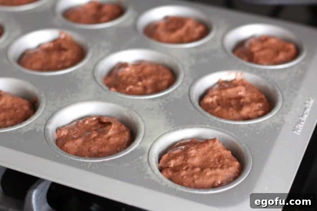 Muffin tin with cups filled with chocolate muffin mix and coconut pecan frosting layers, ready for baking.