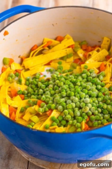 Soul-Warming Chicken and Noodles 13 Milk and frozen peas being stirred into a pot of wide noodles, vegetables, and broth.