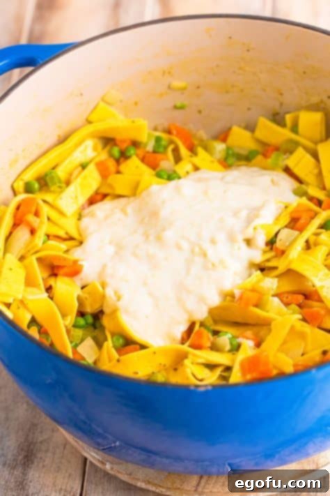 Soul-Warming Chicken and Noodles 15 A creamy roux being poured into the large pot with noodles, vegetables, and broth, ready to thicken the dish.