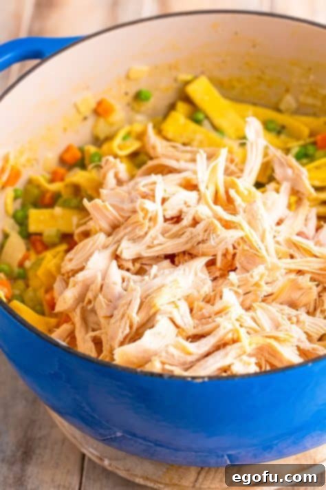 Soul-Warming Chicken and Noodles 16 Shredded chicken being added to the simmering pot containing noodles, vegetables, and thickened broth.