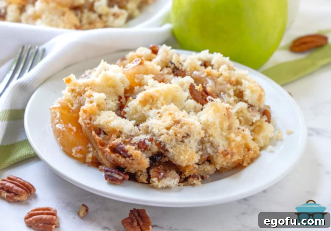 Effortless Apple Crisp 2 A serving of apple crisp on a white plate with a green apple and pecans in the background, showcasing the crispy topping.