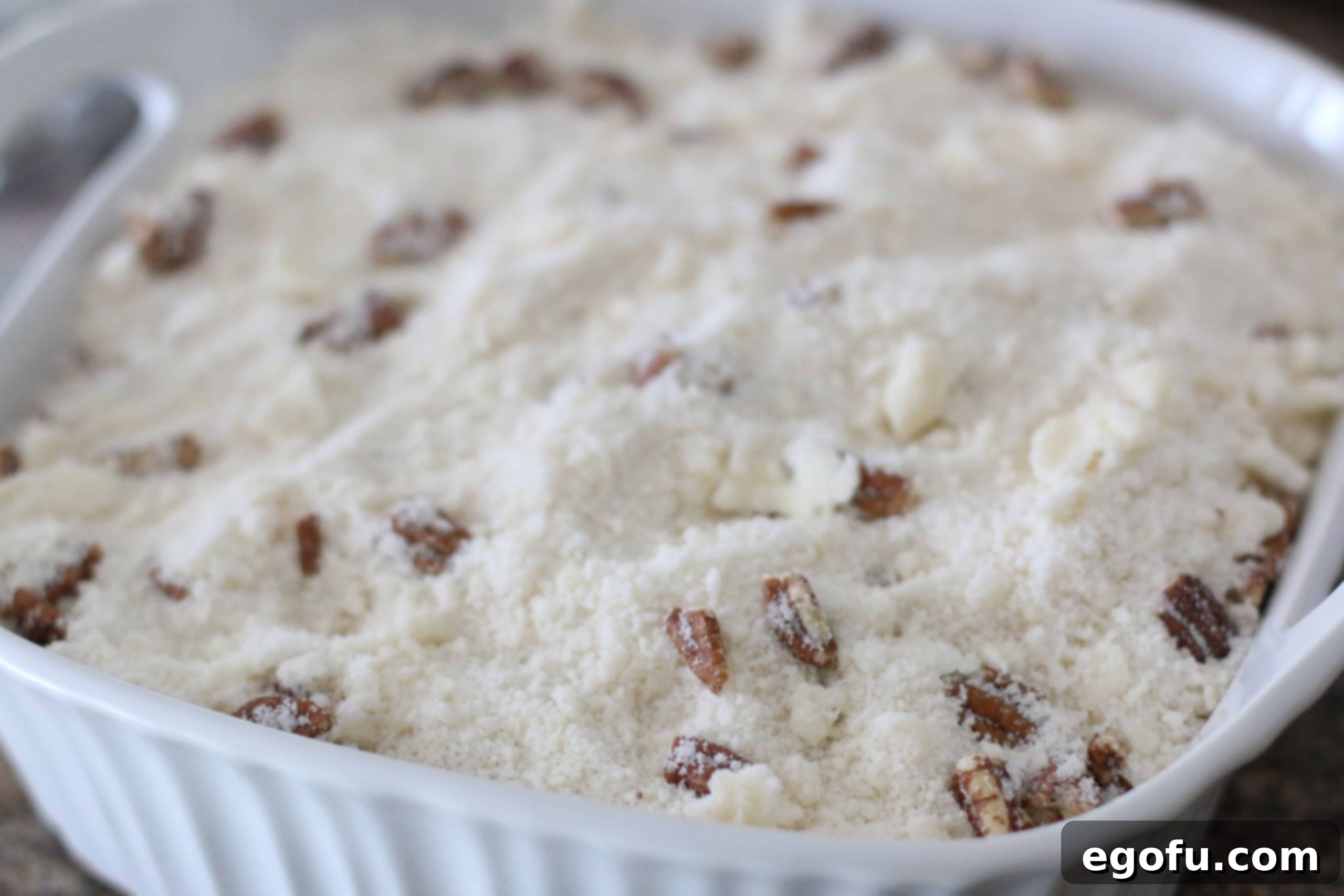 Effortless Apple Crisp 5 Pecan butter crumble topping spread over apple pie filling in a white baking dish before baking.