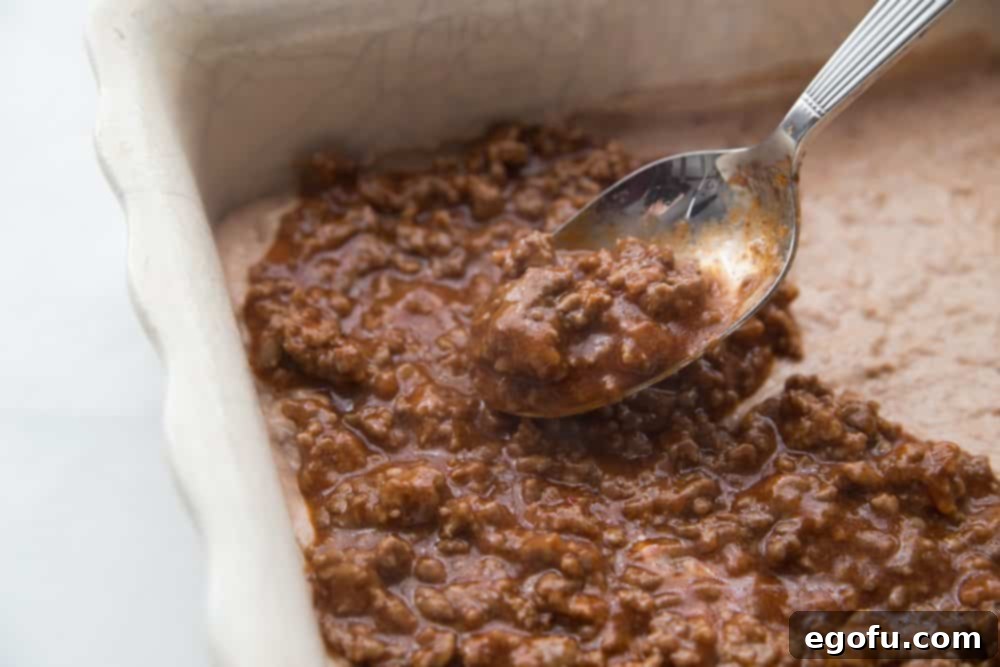 ground beef taco sauce mixture spread over Bisquick mix and refried beans in a square baking dish.
