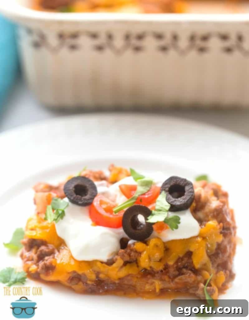 slice, Bisquick Burrito Bake topped with sour cream, lettuce, tomato, sliced olives and sliced green onions.