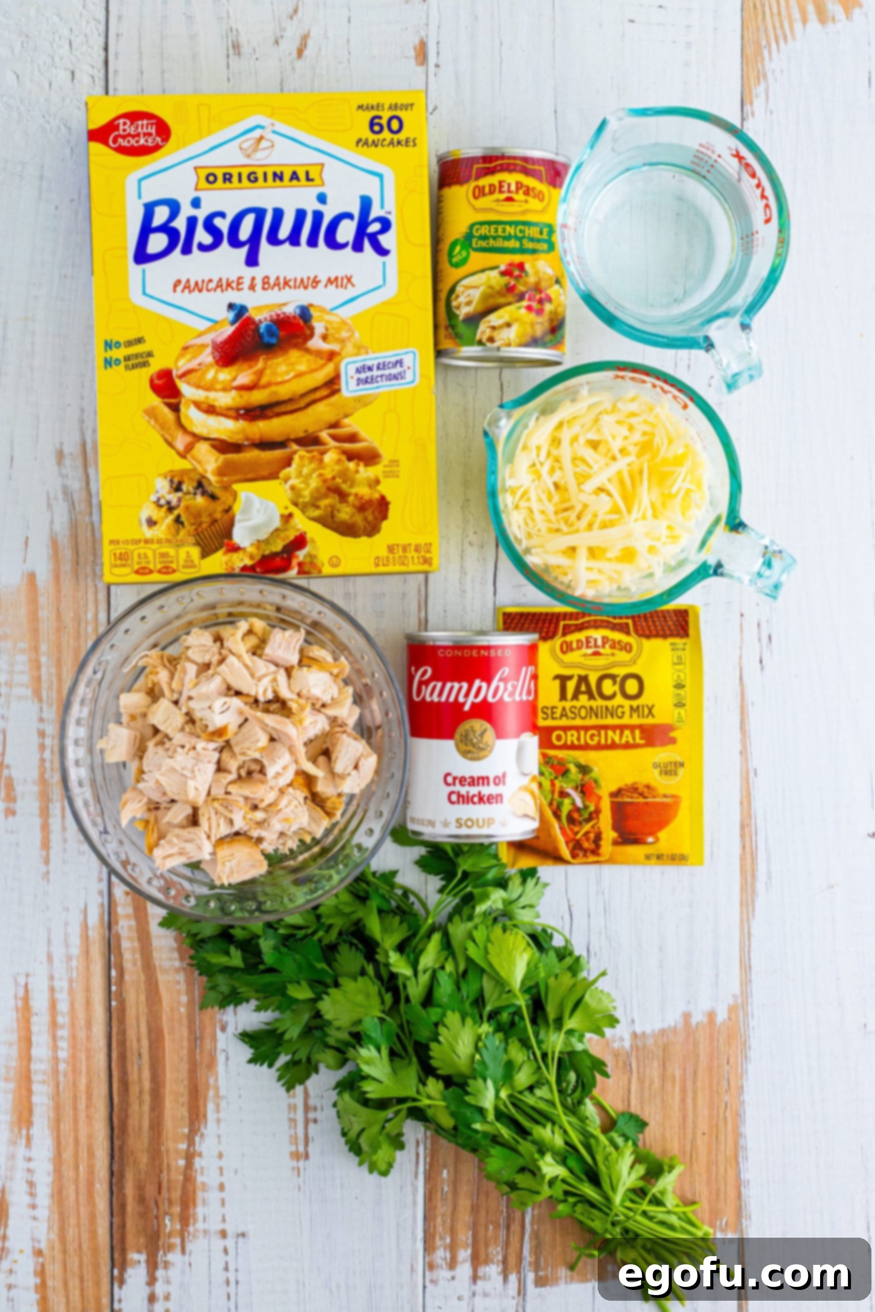 All ingredients laid out: Bisquick mix, cream of chicken soup, taco seasoning, water, enchilada sauce, diced cooked chicken, and shredded Monterey Jack cheese for an easy enchilada bake.