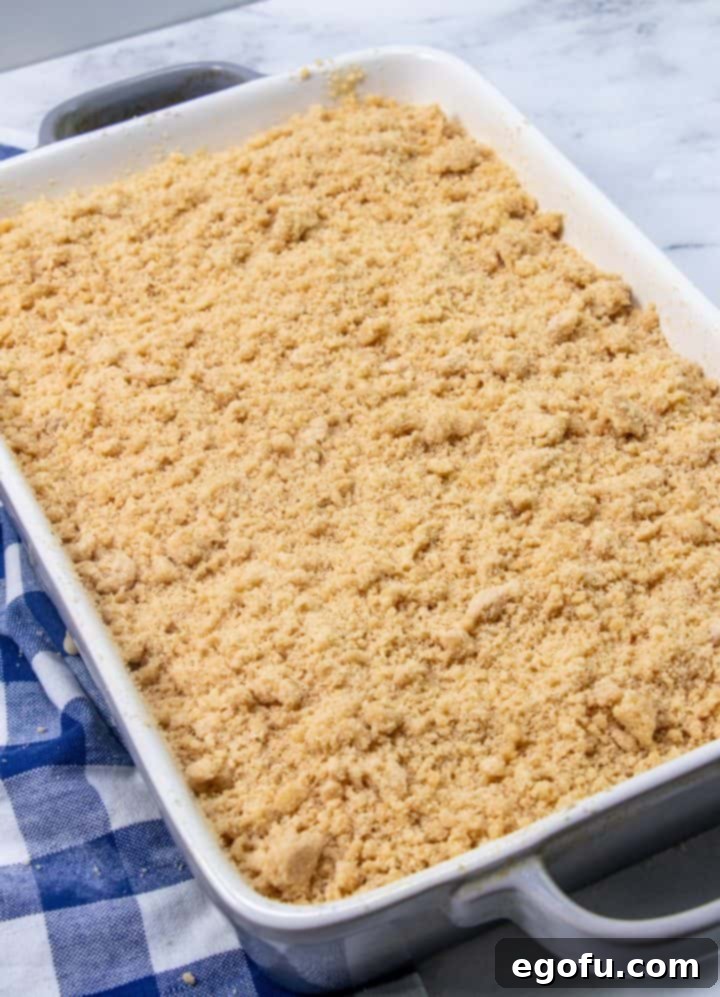 The final layer of crumb mixture beautifully sprinkled over the entire surface of the banana cake batter in the baking dish, ready for baking.