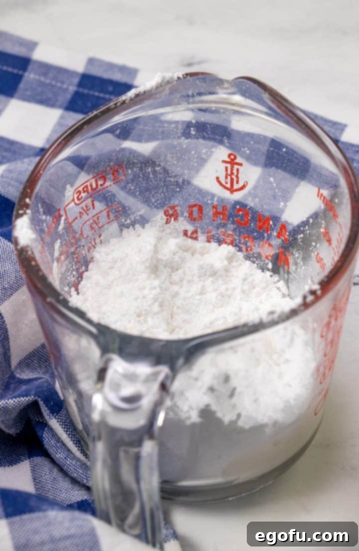 A glass measuring cup containing powdered sugar and milk, whisked together to create a smooth, pourable glaze for the cake.