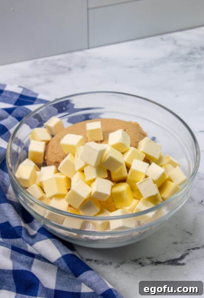 Cold, cubed butter and rich light brown sugar combined in a clear glass bowl, beginning the process of making the crumb topping.