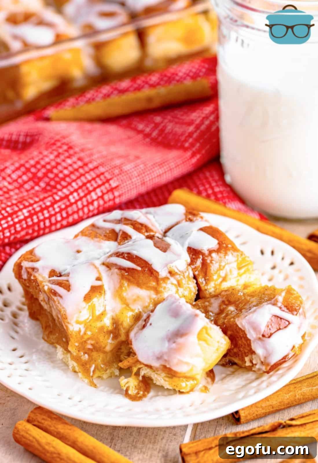 Two rows of beautifully glazed cinnamon pull-apart bread displayed on a pristine white round plate, with a refreshing glass of milk casually blurred in the background, creating a cozy and inviting scene.