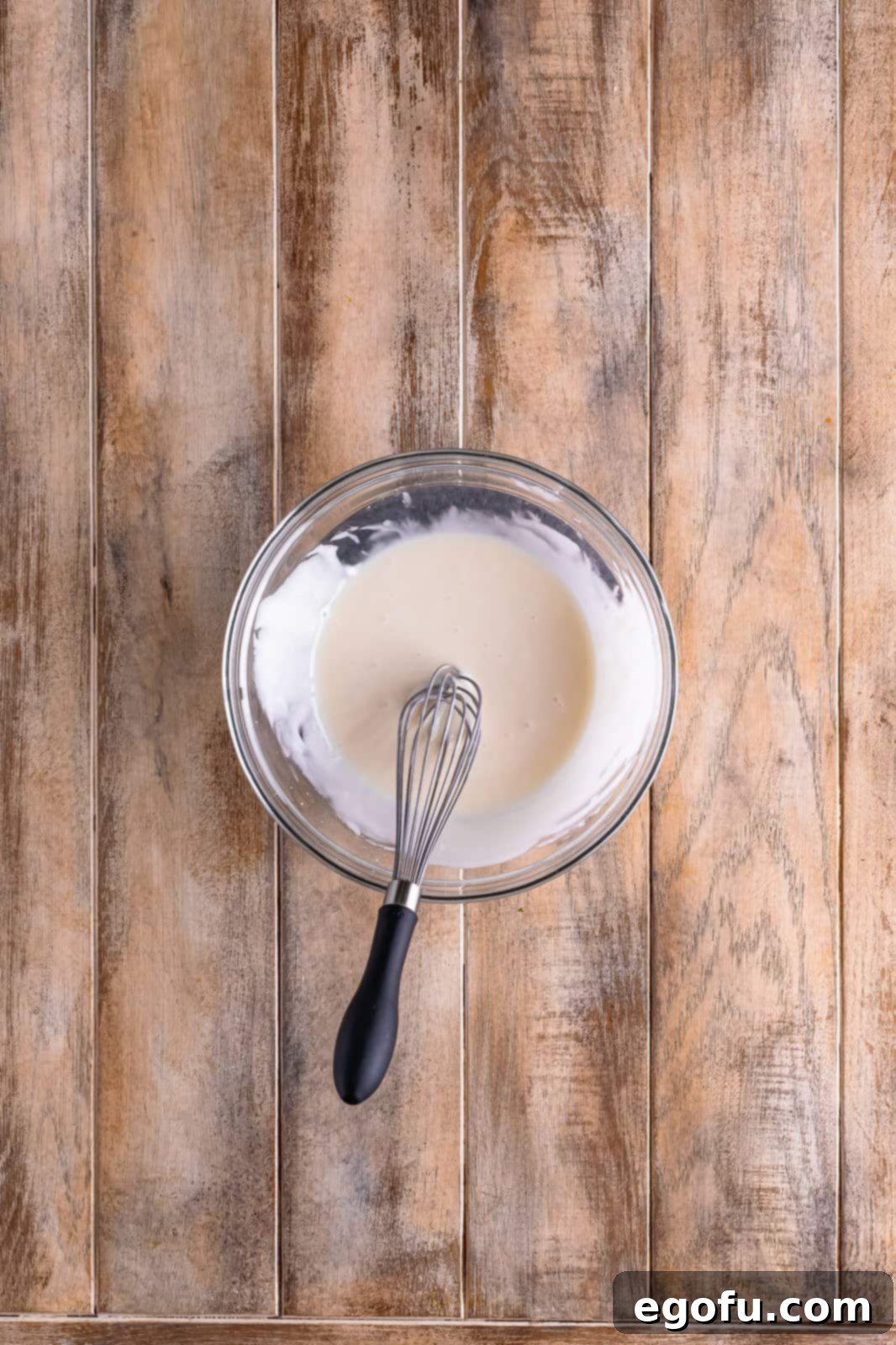 Ingredients for the icing – powdered sugar, milk, and vanilla extract – being whisked together in a bowl to create a smooth, creamy glaze.