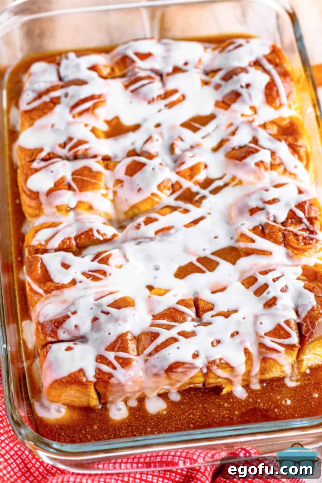 Smooth vanilla icing being generously drizzled over the freshly baked, warm cinnamon pull-apart bread still in its baking dish, creating an inviting visual of sweet indulgence.