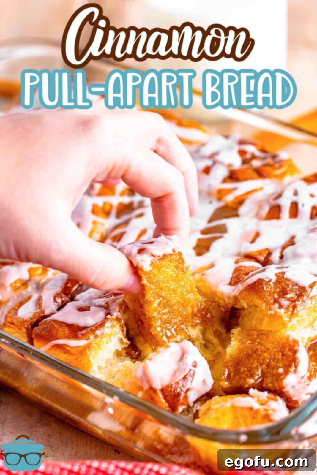 A close-up shot of a hand gently pulling out a small, warm piece of cinnamon pull-apart bread from the baking dish, highlighting its soft, gooey texture and the rich glaze.