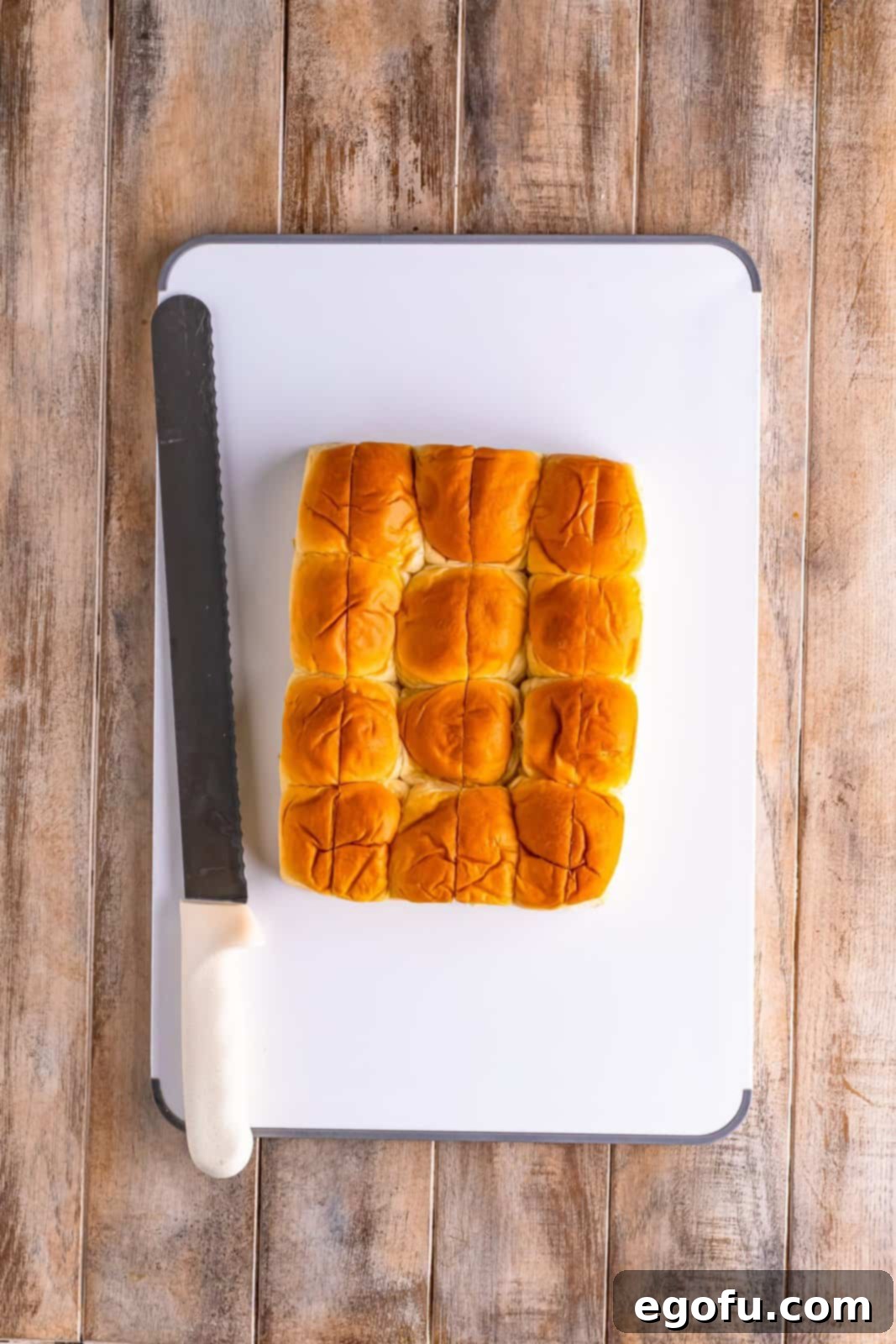 Close-up of a serrated knife making three vertical slices into the top of a King's Hawaiian sweet roll, preparing it for the pull-apart bread recipe.