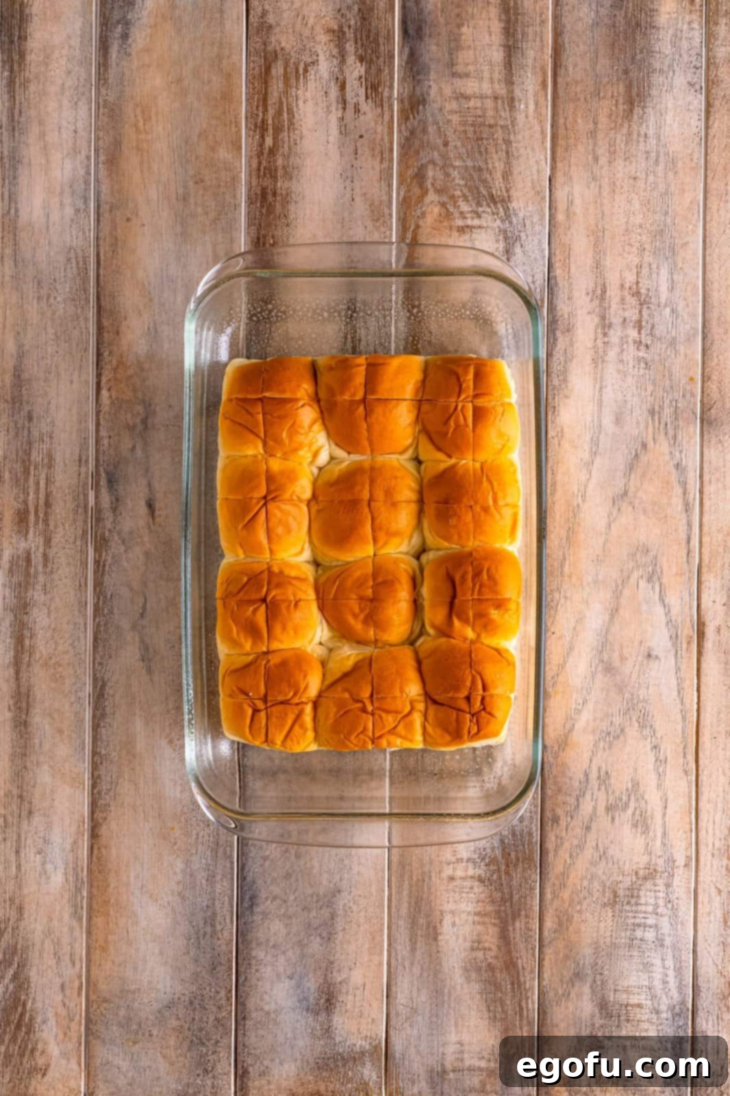 The cross-cut King's Hawaiian sweet rolls carefully arranged in a baking dish, ready to be covered with cinnamon glaze.