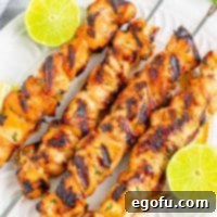 four grilled honey lime chicken skewers on a white plate with sliced fresh limes.