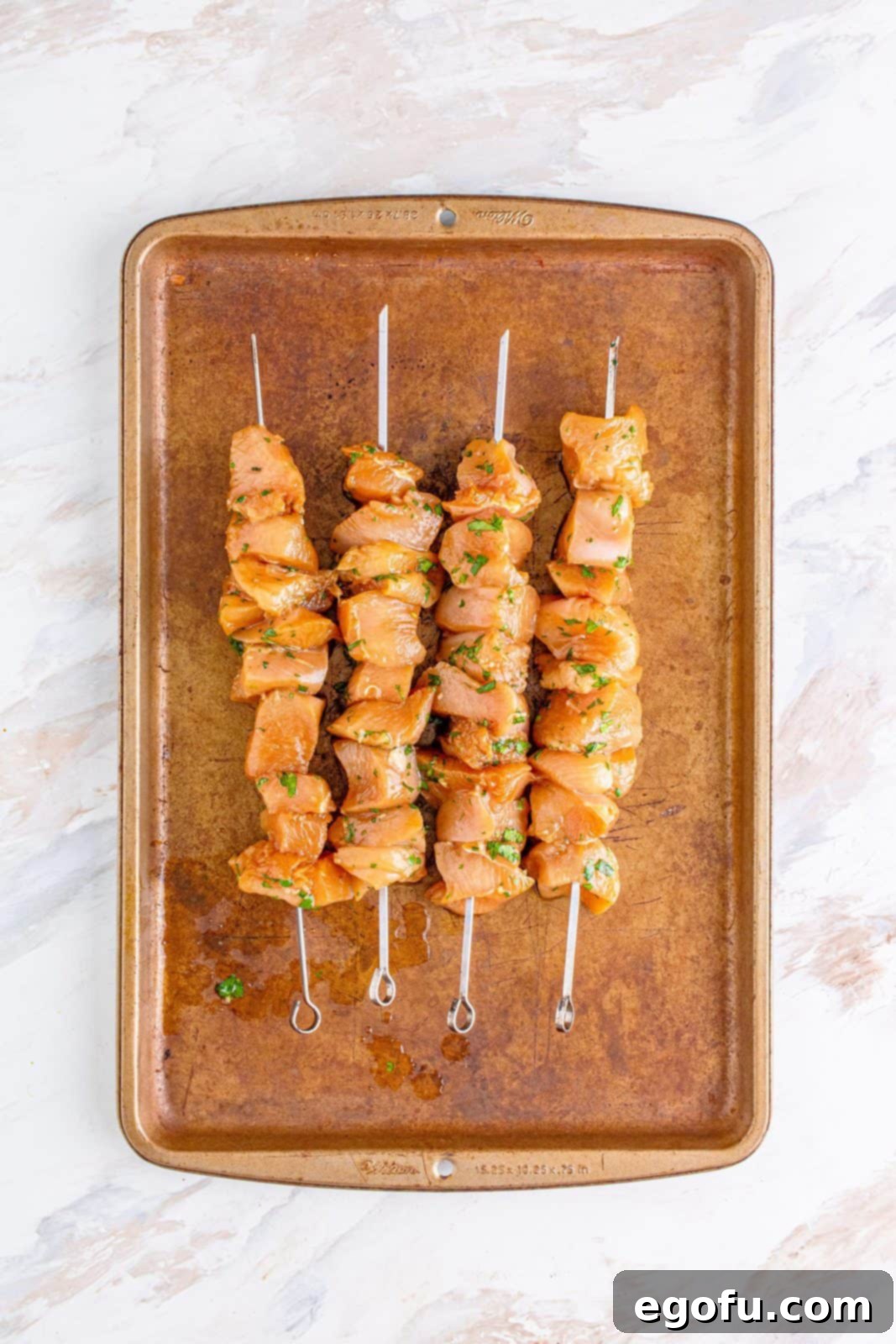 marinated chicken pieces threaded on metal skewers and placed on a baking sheet. 