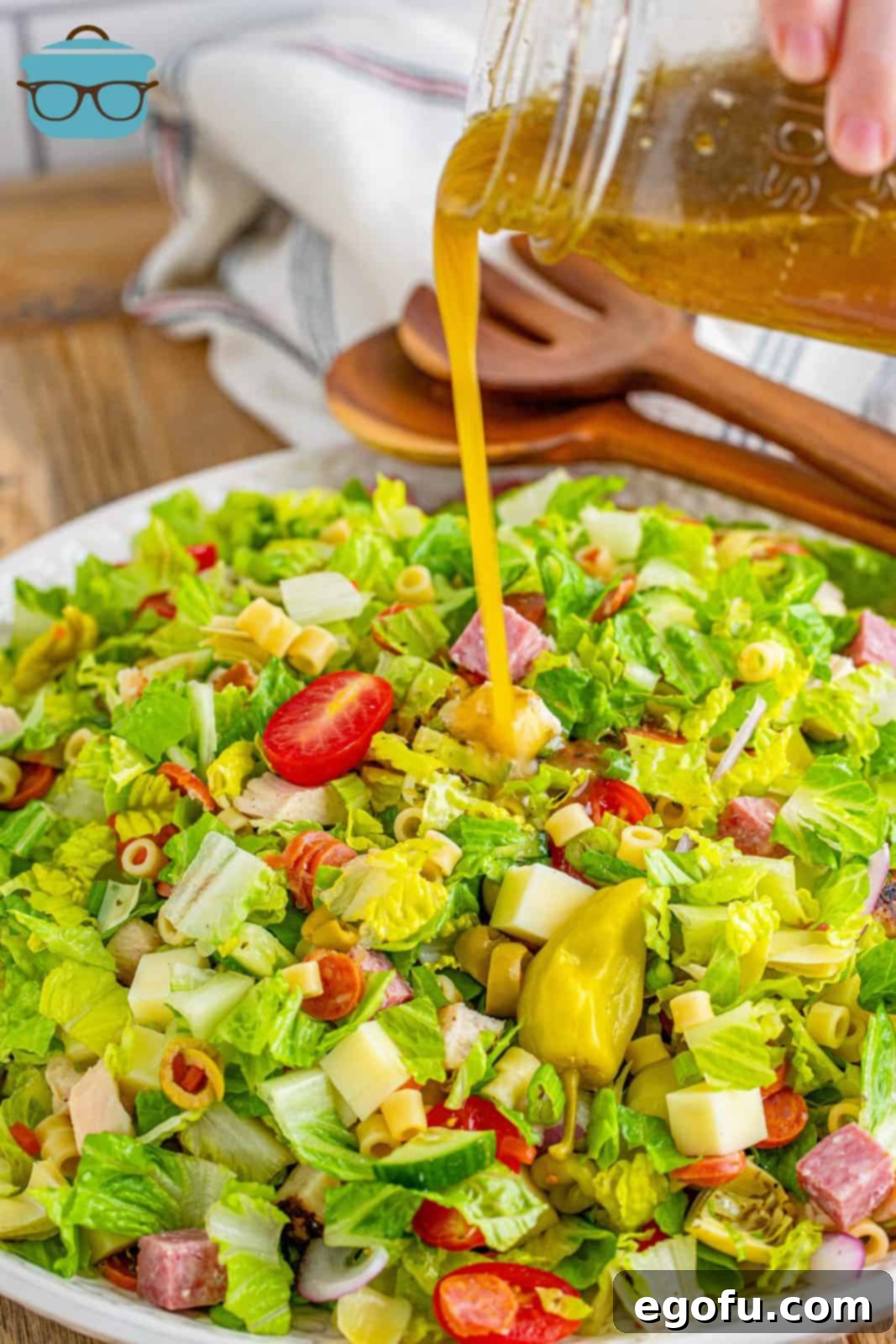 Vibrant Italian Chopped Salad 8 pouring homemade salad dressing from a mason jar over combined salad in a large white bowl.