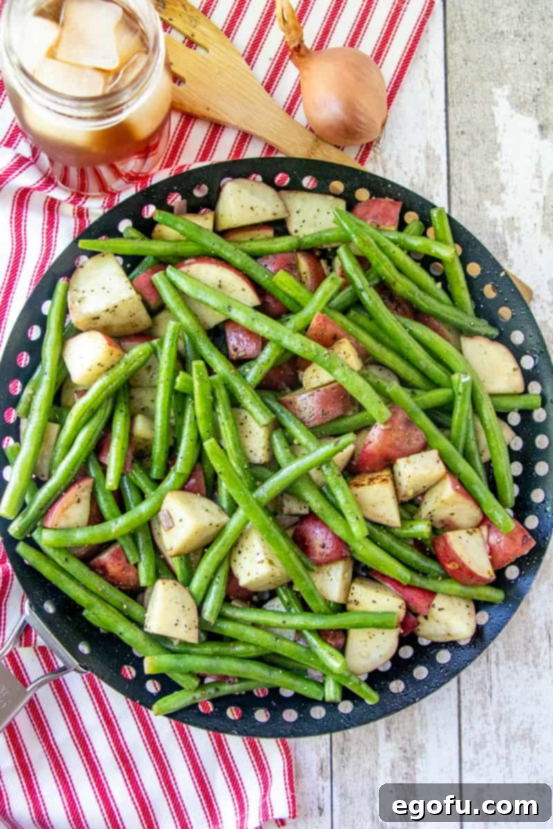 Diced red potatoes and fresh green beans shown in a black grill pan, ready for grilling, with a glass of iced tea off to the side.