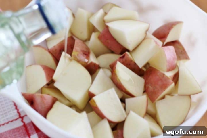 Drizzling olive oil over diced red potatoes in a bowl, preparing them for seasoning.
