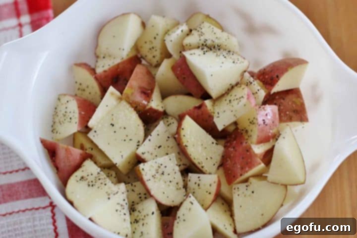 Diced red potatoes shown with lemon pepper seasoning and salt sprinkled on top, ready for mixing.