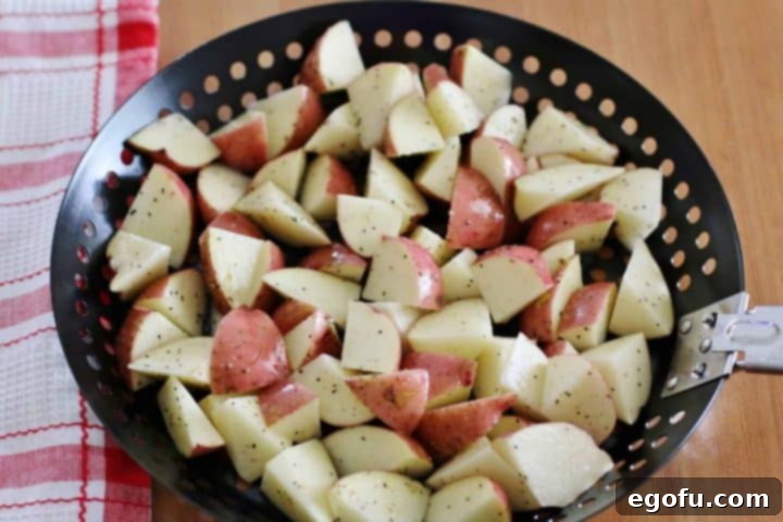 Seasoned and diced red potatoes placed in a round black grill pan, ready for the grill.