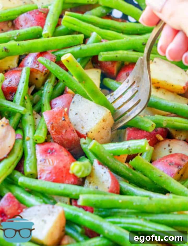 Close-up photo of a fork piercing into a grilled diced potato with green beans in the background, demonstrating tenderness.