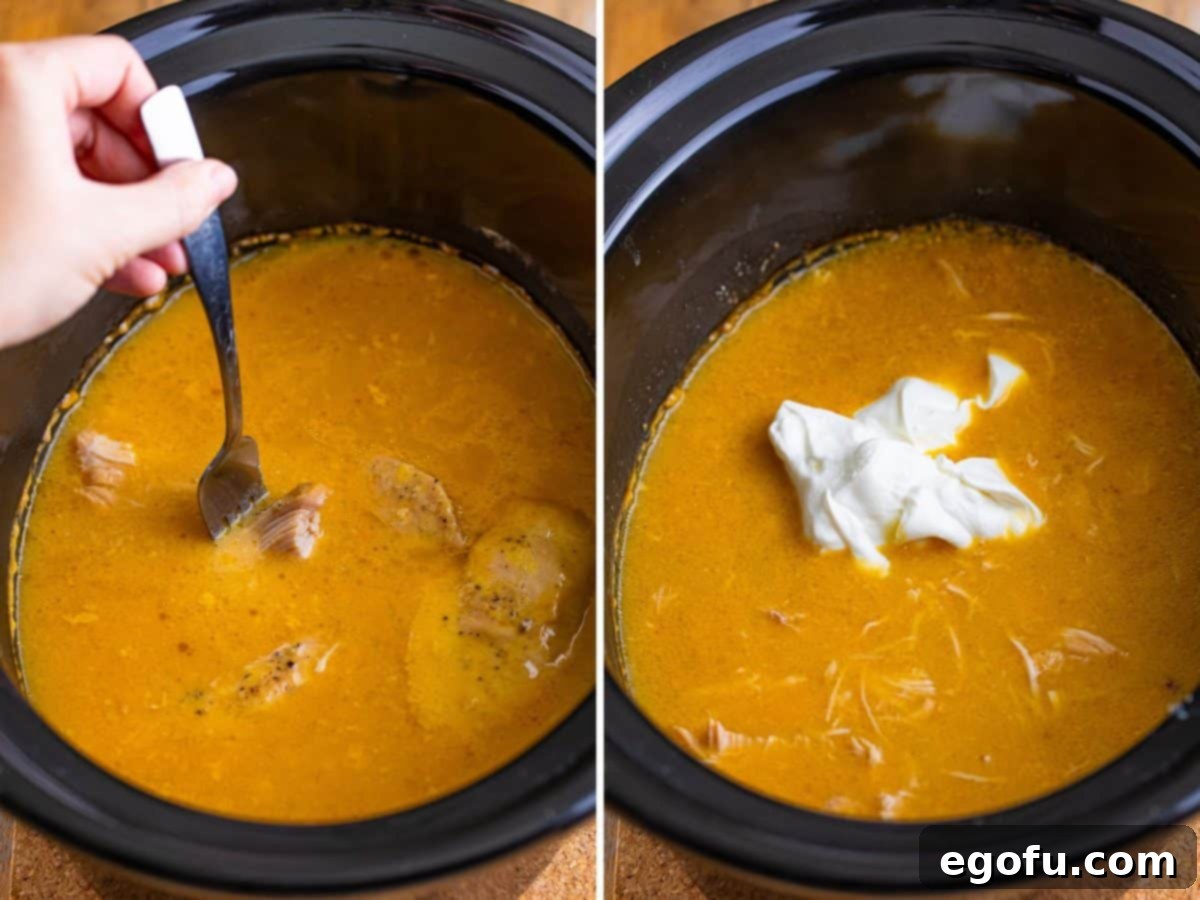 A fork shredding tender chicken in the Crock Pot, and a dollop of sour cream being added to the cooked dish, ready to be stirred in.