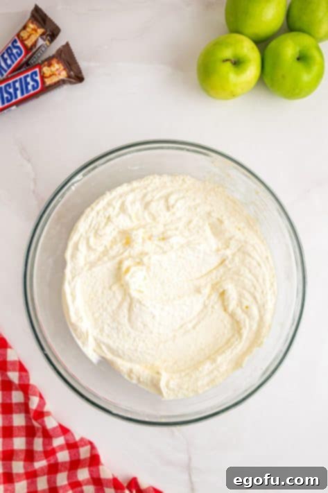 Creamy Snickers Apple Delight 13 Whipped cream being mixed with pudding in a bowl.