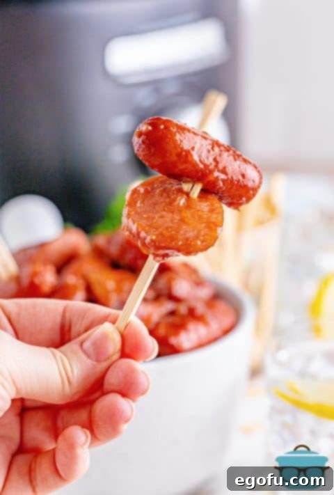 a hand holding up a toothpick holding up two glazed sausage bites.