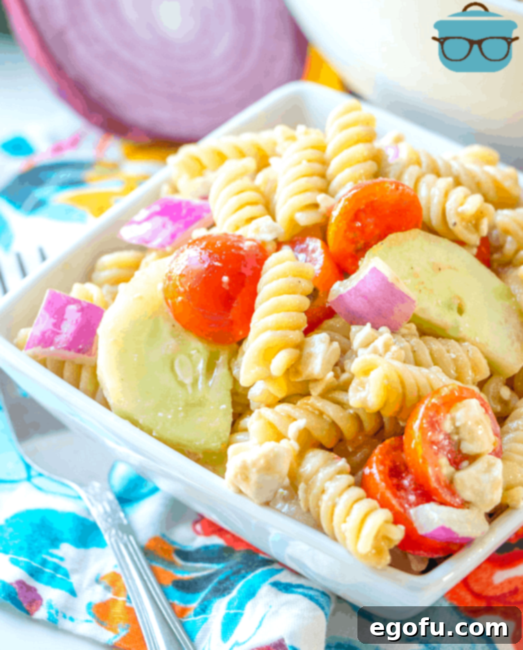 A vibrant rotini pasta salad with sweet balsamic vinegar dressing, crisp cucumbers, juicy cherry tomatoes, and crumbled feta cheese, served in an elegant glass bowl.