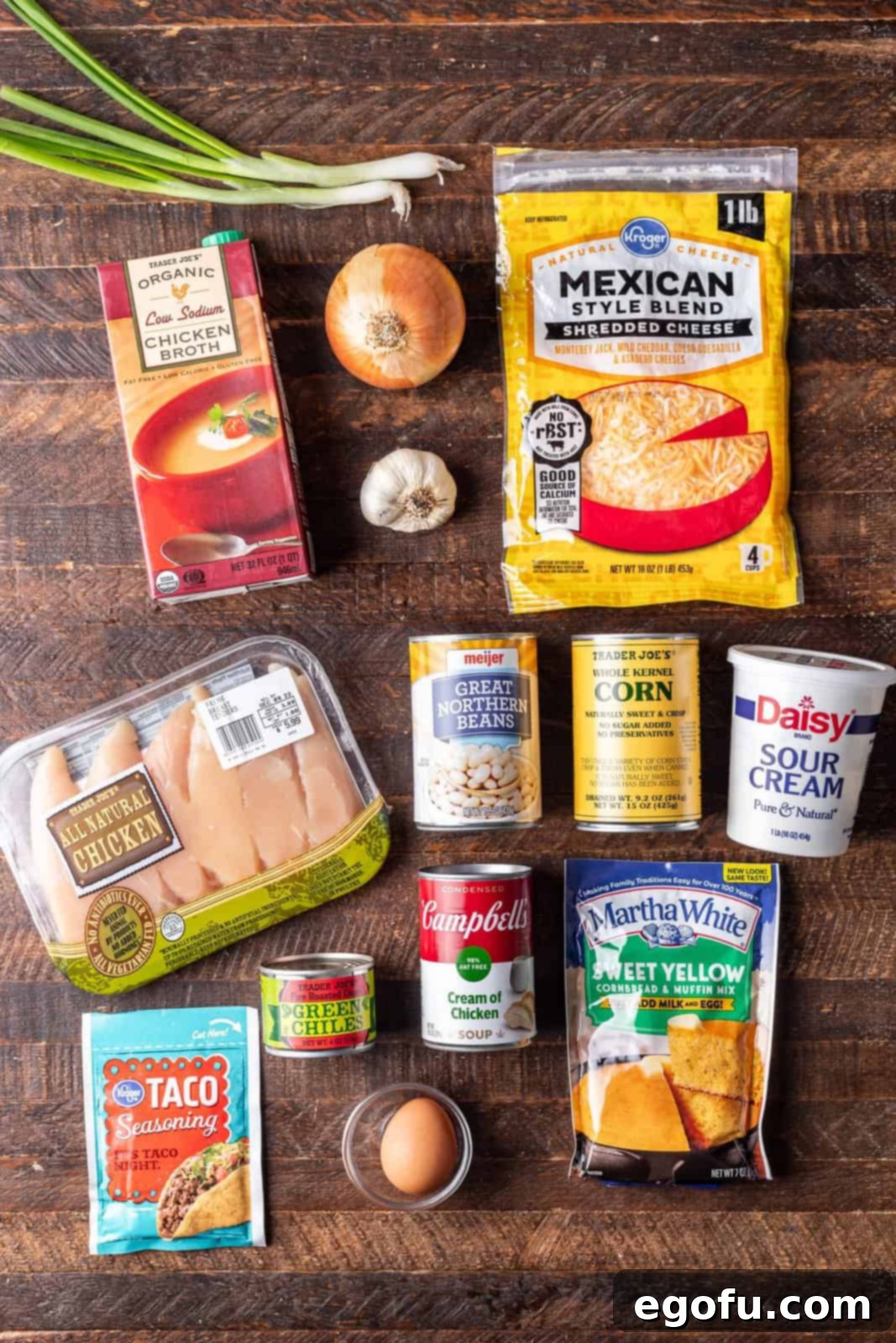 An organized display of ingredients for White Chicken Chili With Cornbread Dumplings, including chicken broth, water, onion, garlic, chicken tenders, taco seasoning, white beans, corn, cream of chicken soup, green chiles, cornbread mix, and green onions.