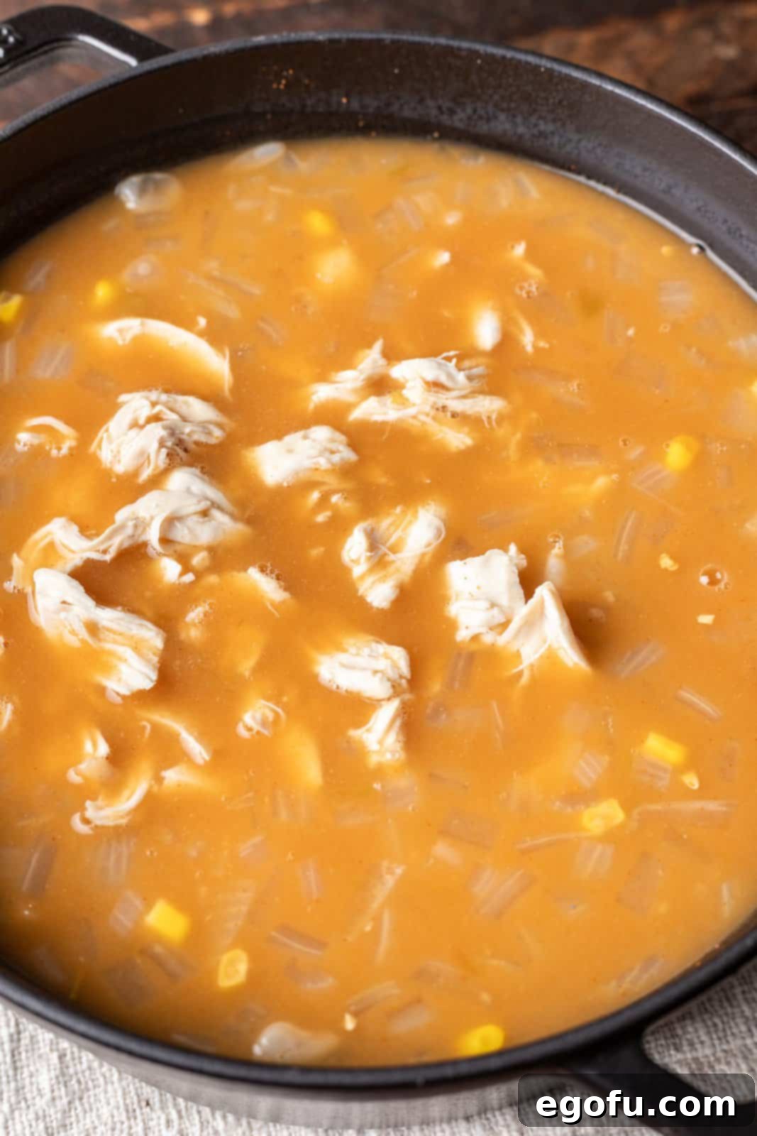 A pot filled with taco seasoning, white beans, corn, cream of chicken soup, green chiles, and shredded chicken, ready to be stirred into the chili. 