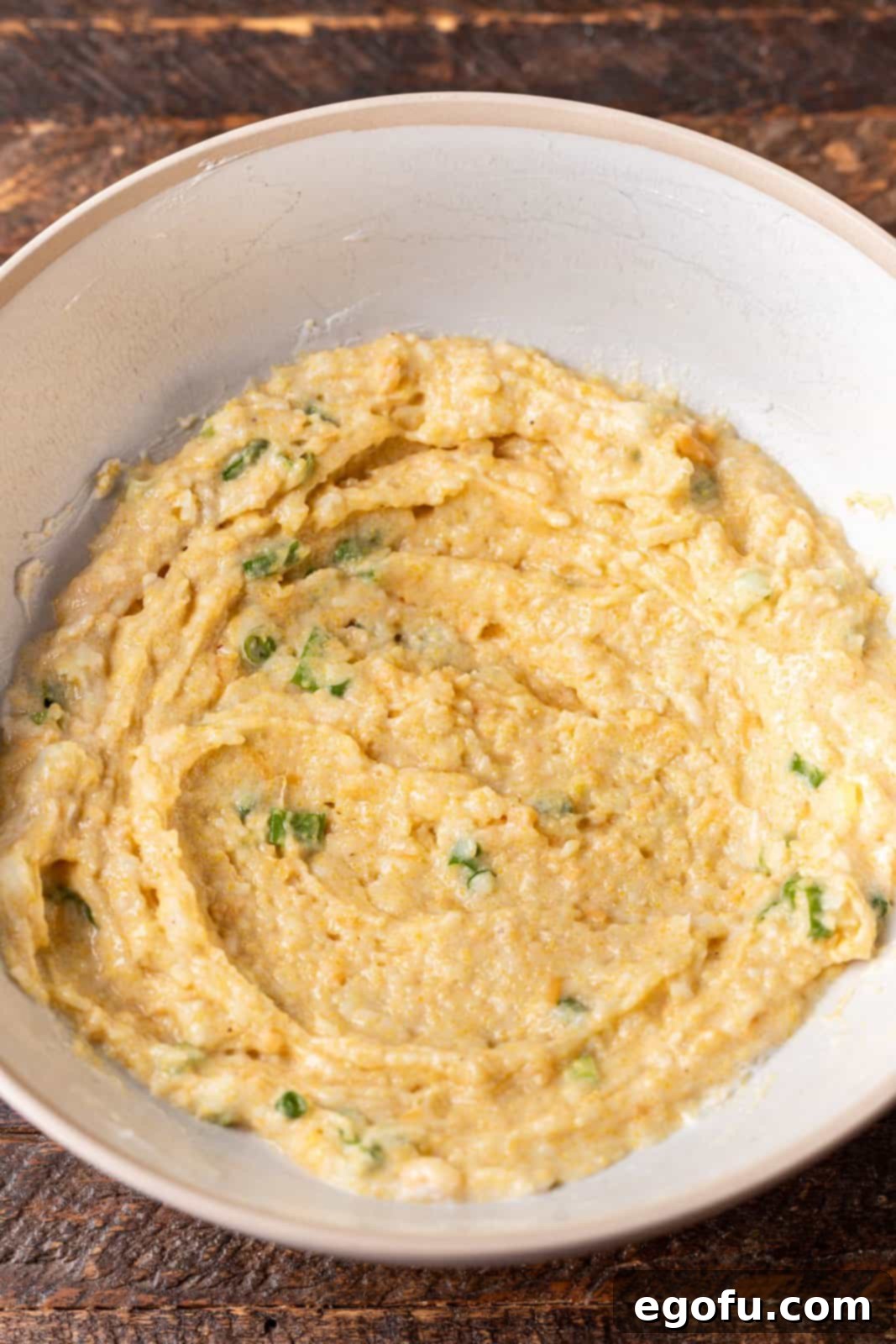 A bowl containing corn muffin mix, green onions, egg, sour cream, and cheese, ready to be combined for the cornbread dumplings. 