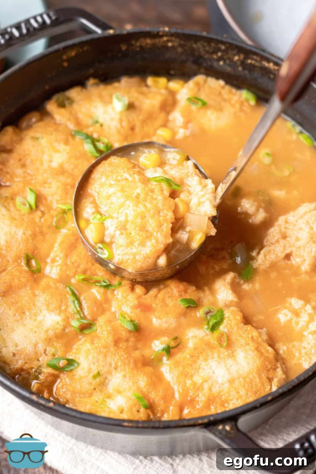 A ladle scooping up tender cornbread dumplings from a large pot of simmering chili, showcasing their fluffy texture. 