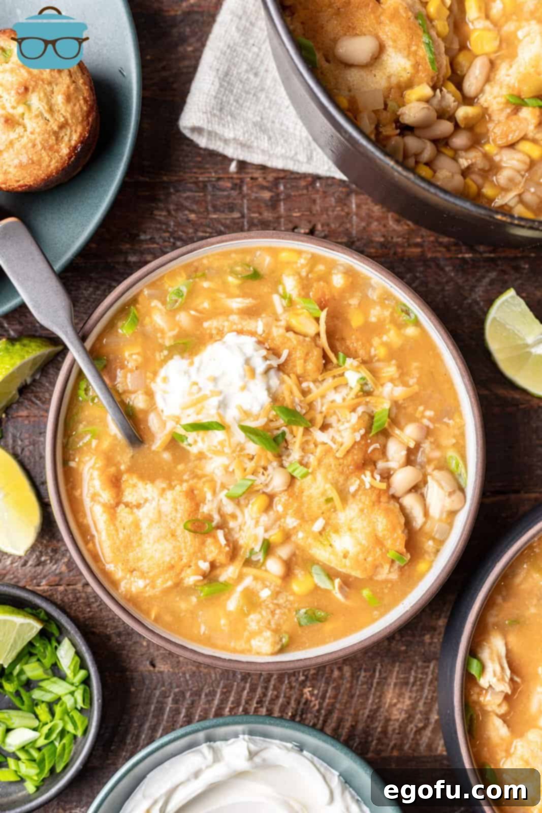 A beautiful bowl of White Chicken Chili with Cornbread Dumplings, generously topped with shredded cheese and a swirl of sour cream, ready to be enjoyed. 