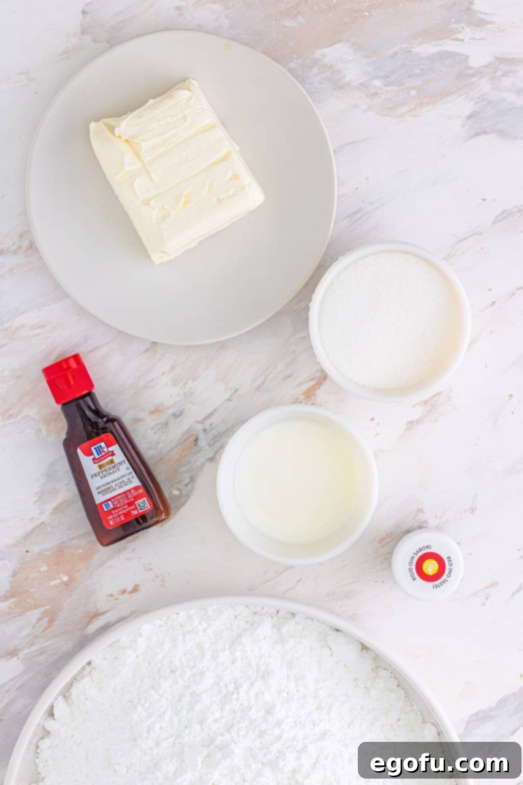 Refreshing Finales 4 Organized shot of all the key ingredients: softened cream cheese, a bottle of mint extract, red food coloring, a bowl of powdered sugar, a small pitcher of milk, and a bowl of granulated sugar.