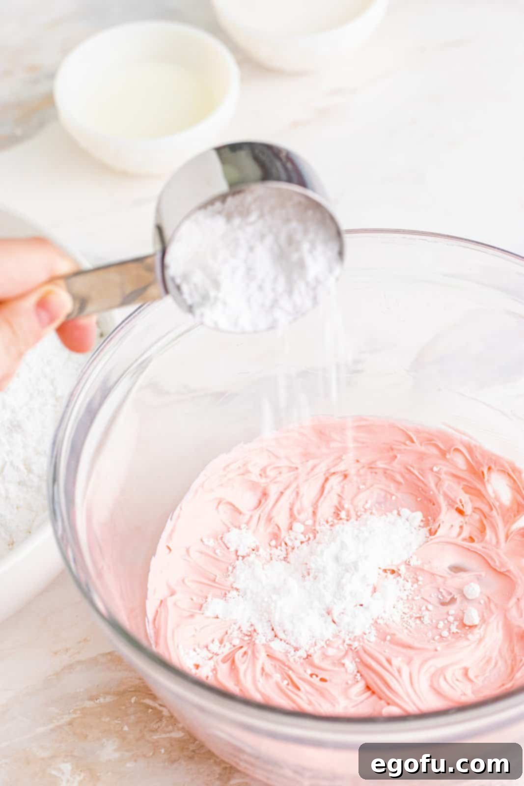 Refreshing Finales 6 Powdered sugar being carefully added to the vibrant red cream cheese and mint mixture in a clear bowl, with some visible white powder.
