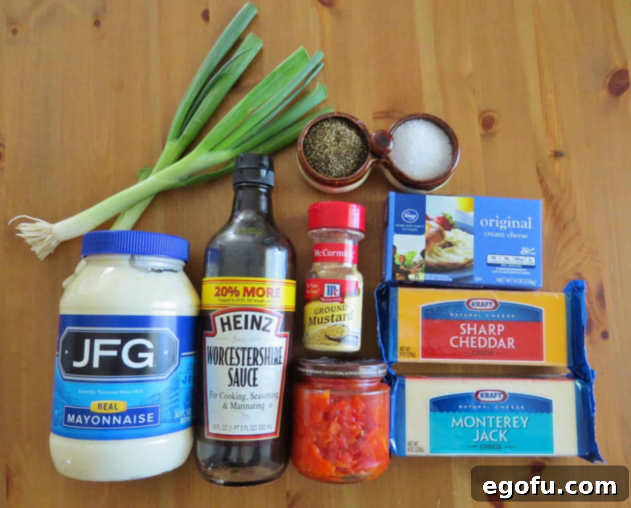 A vibrant flat lay of all the essential ingredients for warm pimiento cheese dip: sharp cheddar, cream cheese, mayonnaise, jar of diced pimientos, chopped green onions, dry mustard, Worcestershire sauce, hot sauce, salt and pepper, and crushed Ritz crackers.