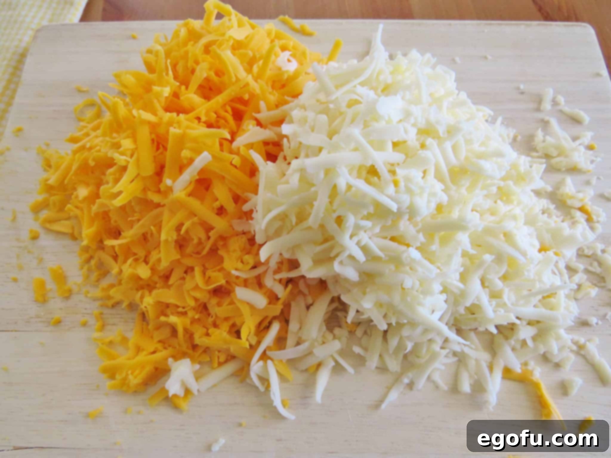 Piles of freshly shredded cheddar and Monterey Jack cheeses on a cutting board, ready for the dip.