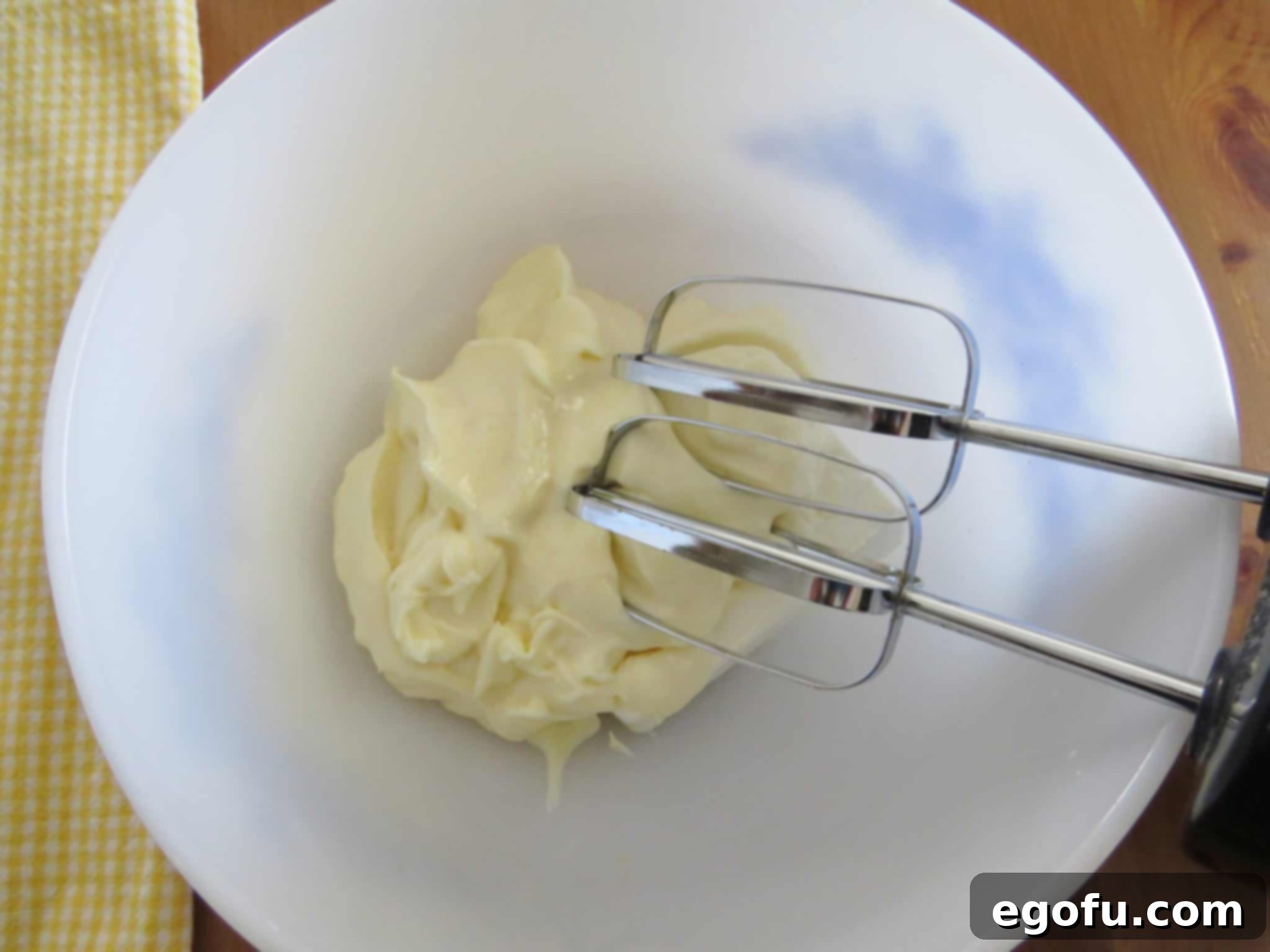 Cream cheese and mayonnaise beautifully mixed together with an electric mixer in a pristine white bowl, forming a smooth base.