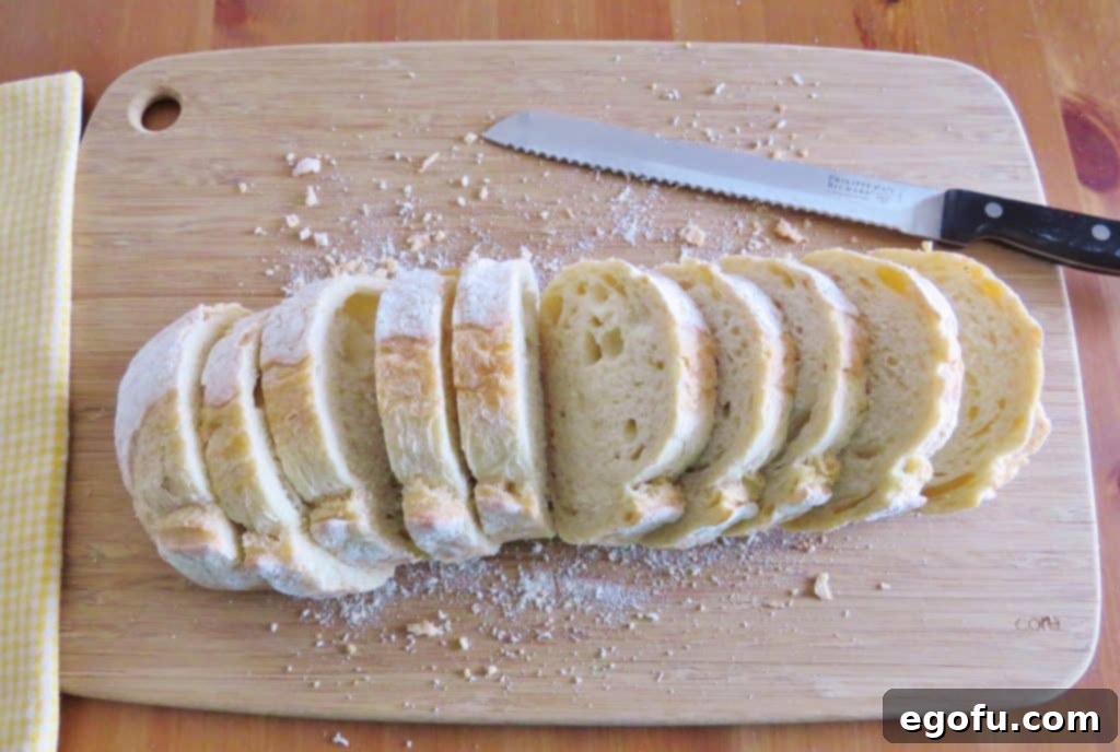 Slices of French bread neatly arranged on a wooden cutting board, ready for preparation.
