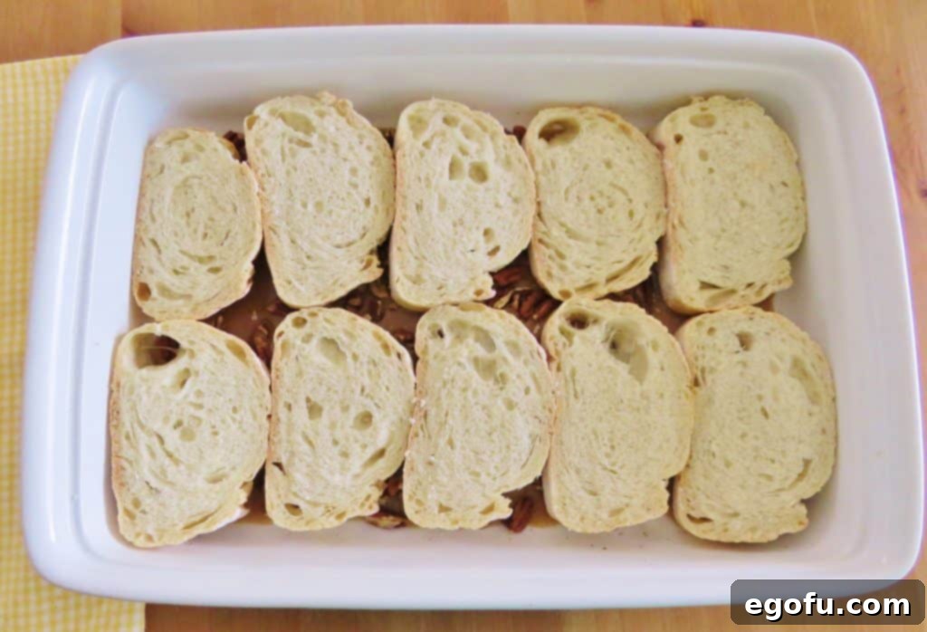 Sliced French bread arranged flat in a white baking dish, ready for the egg mixture.