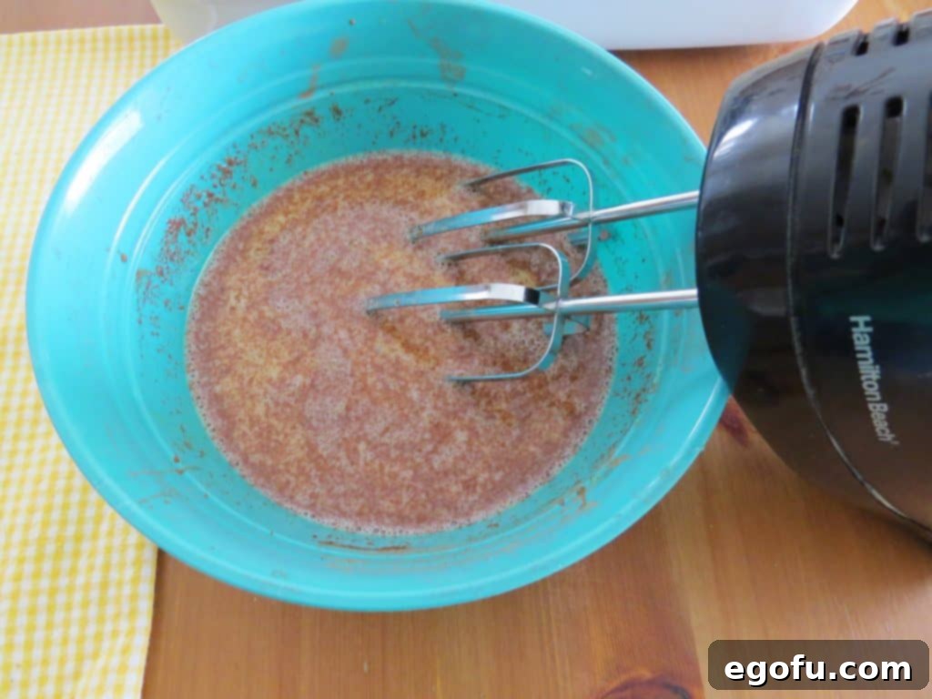 French toast custard mixture being thoroughly combined in a blue bowl using an electric hand mixer.