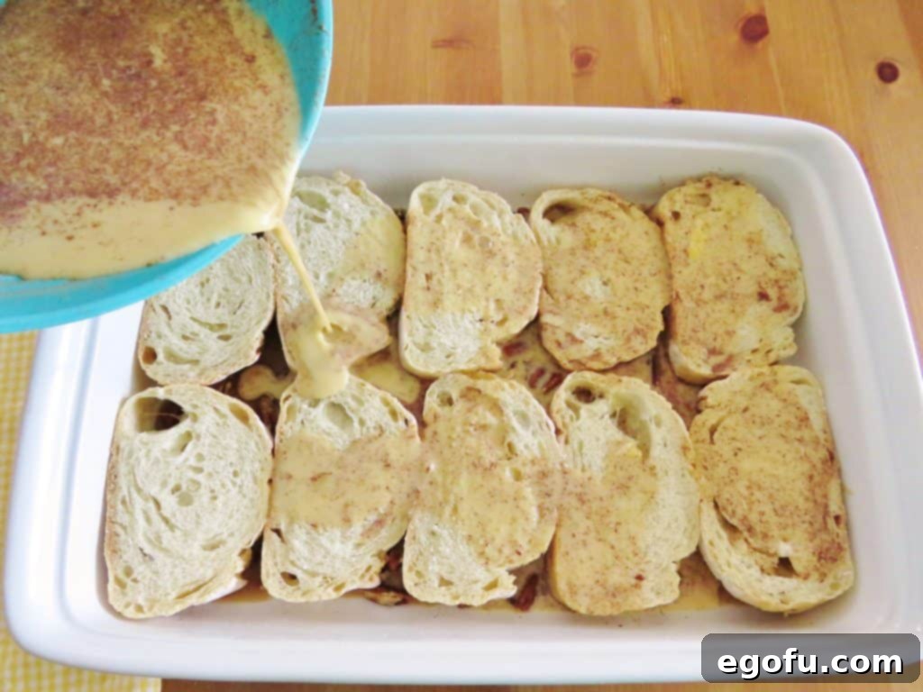 Pouring the creamy egg mixture evenly over the sliced French bread pieces in the casserole dish.