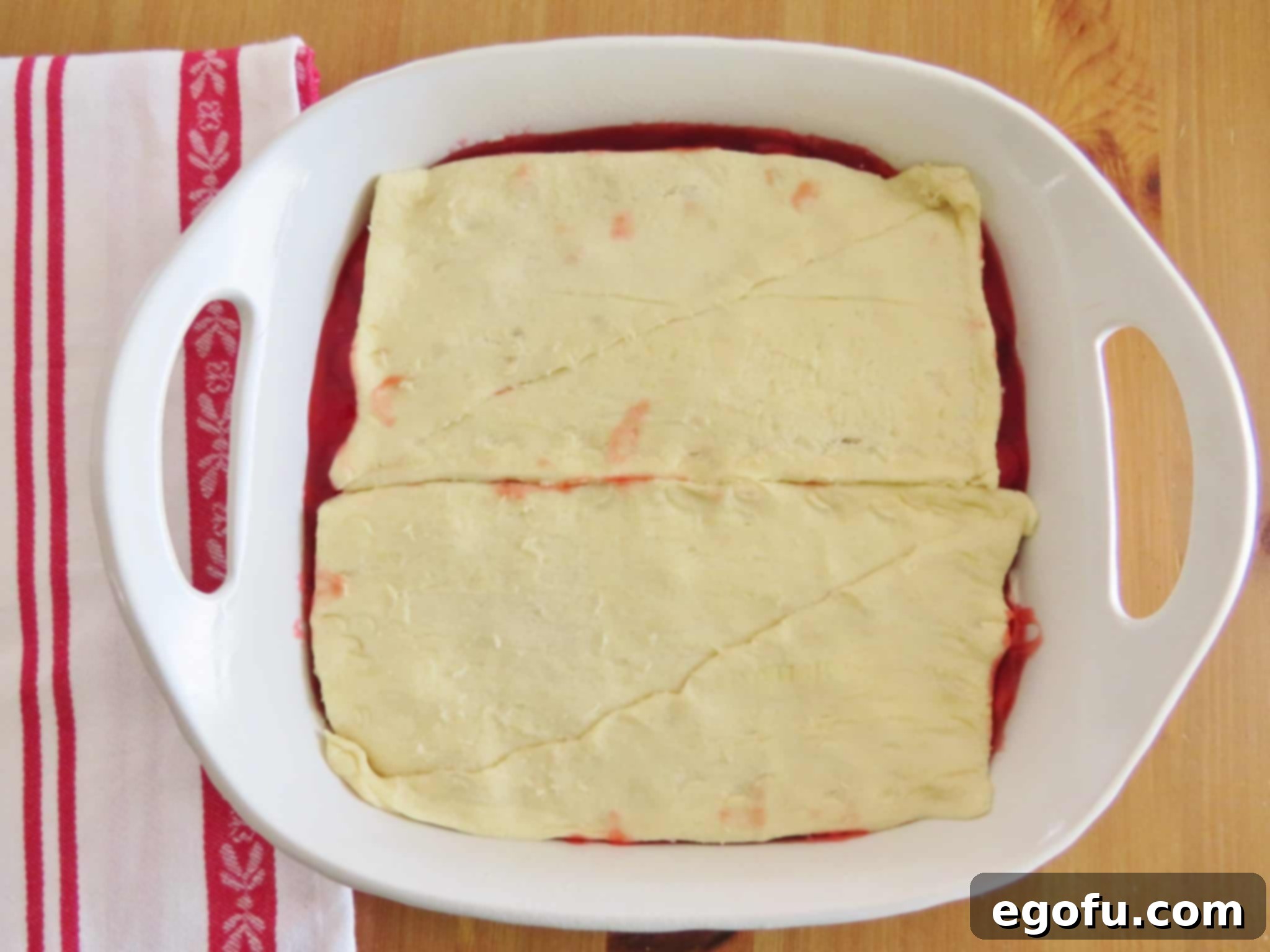 laying crescent roll dough on top of cheesecake and cherry pie filling layers.