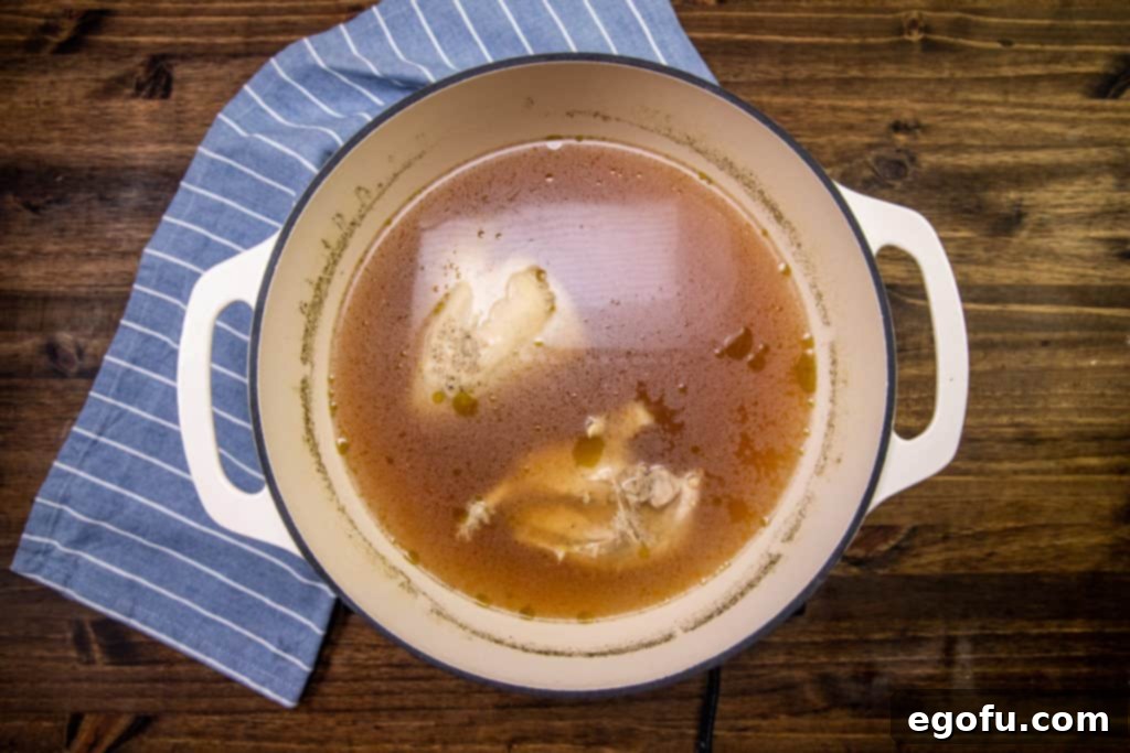 Fully cooked chicken simmering in a rich chicken broth in a stock pot.