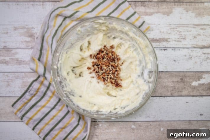 chopped pecans added to cream cheese frosting in bowl.